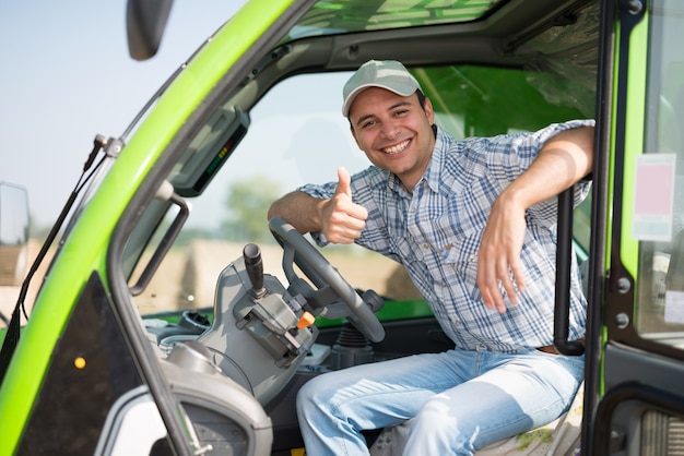 Porträt eines lächelnden landwirts, der daumen in seinem traktor gibt