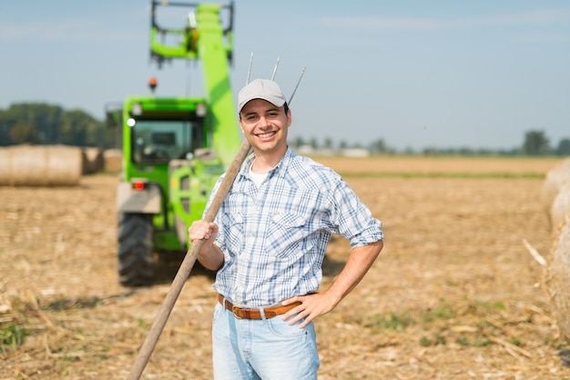 Foto porträt eines lächelnden landwirts, der eine heugabel beim arbeiten auf seinem gebiet hält