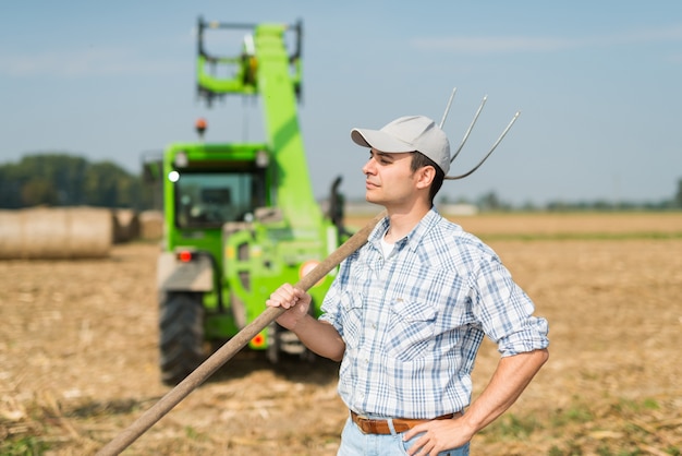 Porträt eines lächelnden Landwirts, der eine Heugabel beim Arbeiten auf seinem Gebiet hält