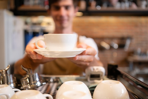 Foto porträt eines lächelnden männlichen baristas, der eine tasse kaffee hält