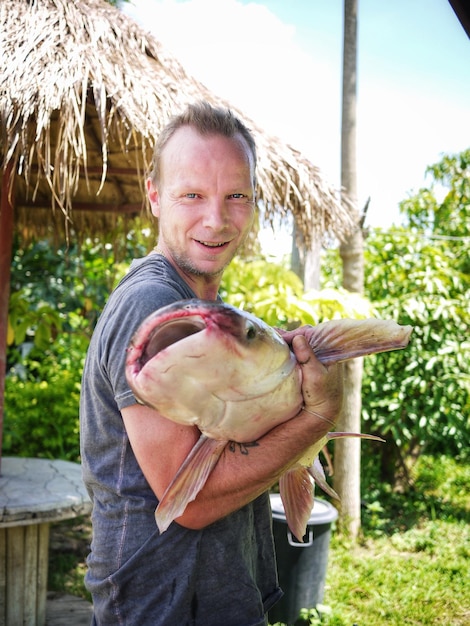 Foto porträt eines lächelnden mannes, der toten fisch im freien hält