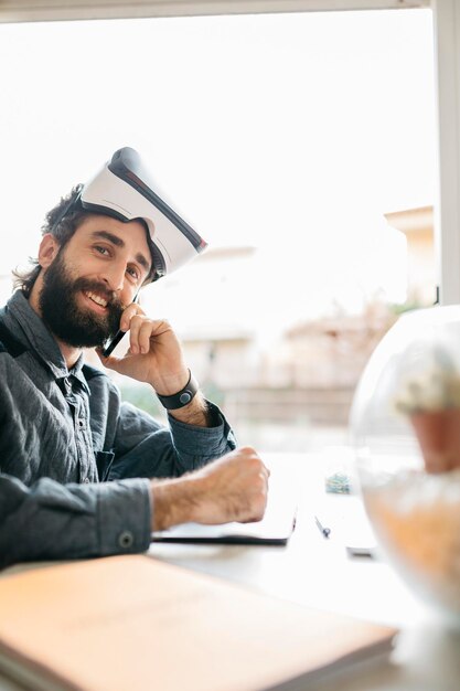 Porträt eines lächelnden Mannes mit Virtual-Reality-Brille am Telefon in seinem Büro