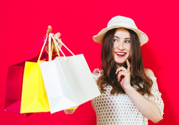 Porträt eines lächelnden netten Mädchens, das Einkaufstaschen hält und Kreditkarte über Rot zeigt