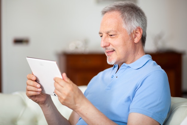 Porträt eines lächelnden reifen Mannes, der sein digitales Tablett beim Sitzen auf der Couch verwendet