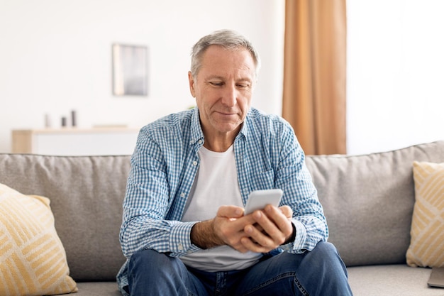 Porträt eines lächelnden reifen Mannes mit Smartphone zu Hause