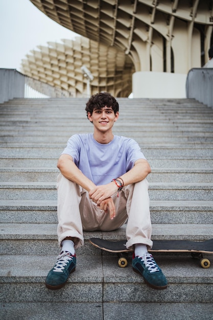 Porträt eines lächelnden Skaterjungen, der auf der Treppe sitzt, während er sich ausruht