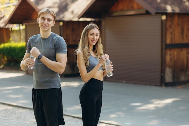 Porträt eines lächelnden Sportpaares, das Wasserflaschen im Park hält