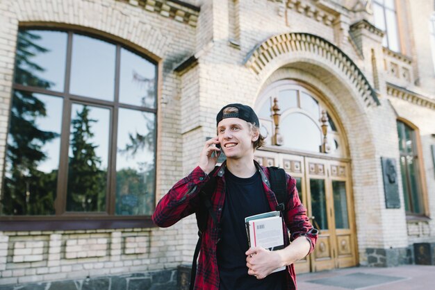 Porträt eines lächelnden Studenten mit Büchern in seinen Händen, die am Telefon sprechen