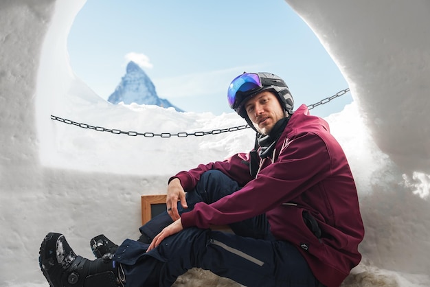 Porträt eines lächelnden Touristen-Snowboarders, der in einem Iglu-Dorf mit Aussicht sitzt