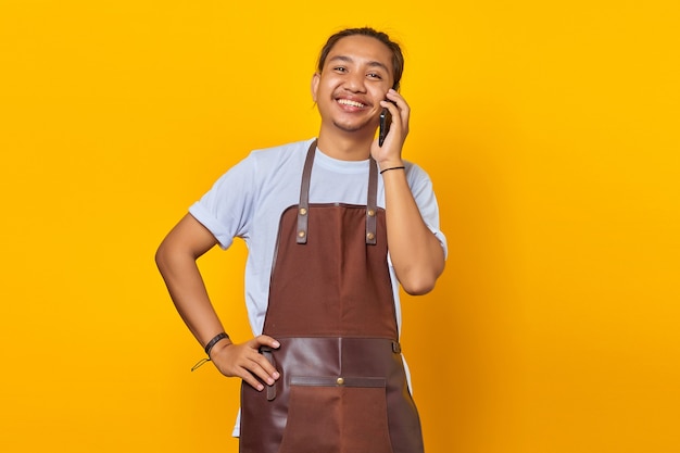 Porträt eines lächelnden und fröhlichen asiatischen jungen Mannes, der auf gelbem Hintergrund auf dem Smartphone spricht