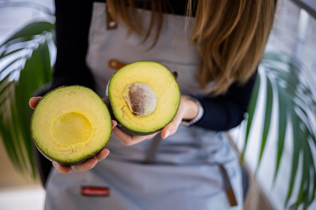 Porträt eines lächelnden Verkäufers der jungen Frau in der Schürze, die zwei Hälften der frischen reifen grünen Avocado hält