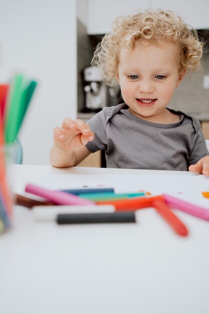 Porträt eines lächelnden Vorschulmädchens, das an ihrem Küchentisch sitzt und mit Plastilin spielt