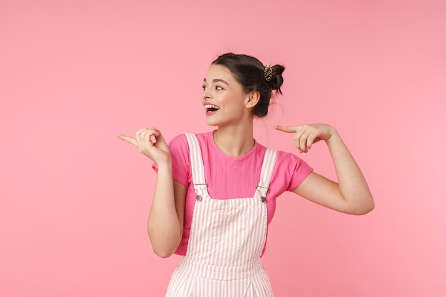 Porträt eines lustigen charmanten Mädchens mit Nasenring, der mit den Fingern zur Seite zeigt und über rosafarbener Wand isoliert lacht