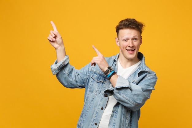 Porträt eines lustigen jungen Mannes in Denim-Freizeitkleidung, der mit dem Zeigefinger nach oben zeigt, isoliert auf gelb-orangefarbenem Wandhintergrund im Studio. Menschen aufrichtige Emotionen Lifestyle-Konzept. Mock-up-Kopienbereich.