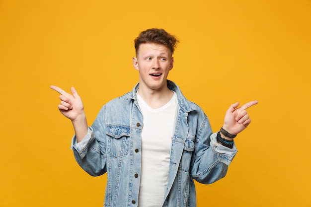 Porträt eines lustigen jungen Mannes in Denim-Freizeitkleidung, der mit dem Zeigefinger zur Seite zeigt, isoliert auf gelb-orangefarbenem Wandhintergrund. Menschen aufrichtige Emotionen, Lifestyle-Konzept. Mock-up-Kopienbereich.