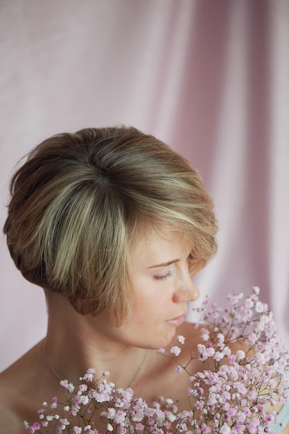 Porträt eines Mädchens auf einem rosa Hintergrund mit Blumen Zärtlichkeit und Weiblichkeit Die Sphäre der Schönheit und der Gesundheit der Frauen Kurzhaarschnitt blonde Haare