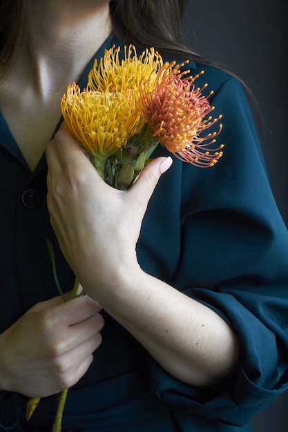 Porträt eines Mädchens, das drei gelbe und orange Proteas hält