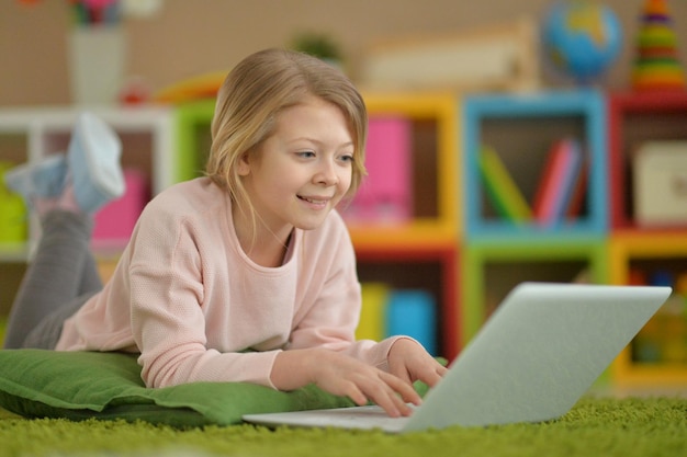 Porträt eines Mädchens, das einen modernen Laptop benutzt, während es auf dem Boden liegt