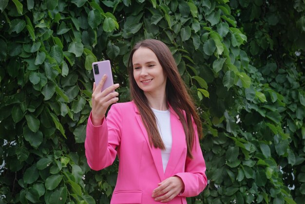 Porträt eines Mädchens im Freien Eine glückliche lächelnde Studentin macht ein Selfie mit einem Smartphone vor dem Hintergrund eines Sommer- oder Herbstparks