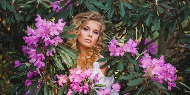 Porträt eines Mädchens in einem blühenden Garten Ein Blumenstrauch ist Rhododendron-Rosa Schönes Haar und Make-up