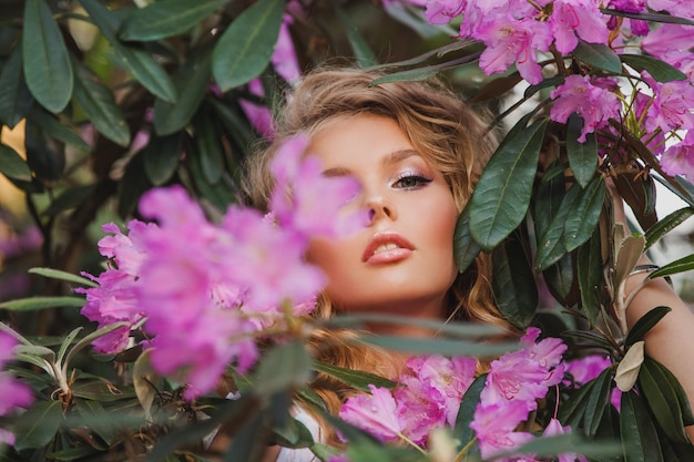 Porträt eines Mädchens in einem blühenden Garten Ein Blumenstrauch ist Rhododendron-Rosa Schönes Haar und Make-up