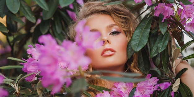 Porträt eines Mädchens in einem blühenden Garten Ein Blumenstrauch ist Rhododendron-Rosa Schönes Haar und Make-up