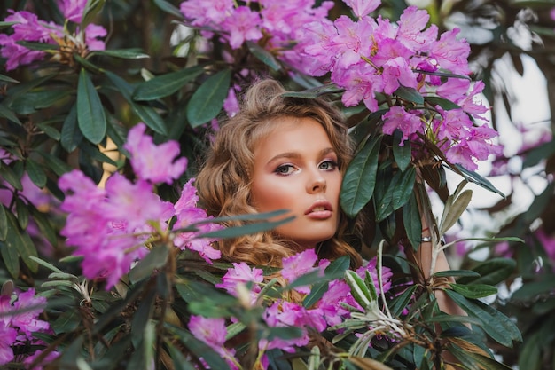 Porträt eines Mädchens in einem blühenden Garten Ein Blumenstrauch ist Rhododendron-Rosa Schönes Haar und Make-up