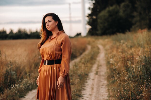 Porträt eines Mädchens in einem orangefarbenen langen Kleid mit langen Haaren in der Natur am Abend.