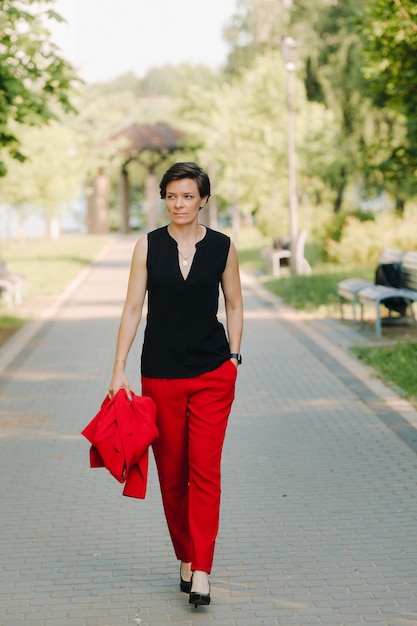 Porträt eines Mädchens in einem roten Anzug, das in der Gasse des Parks steht