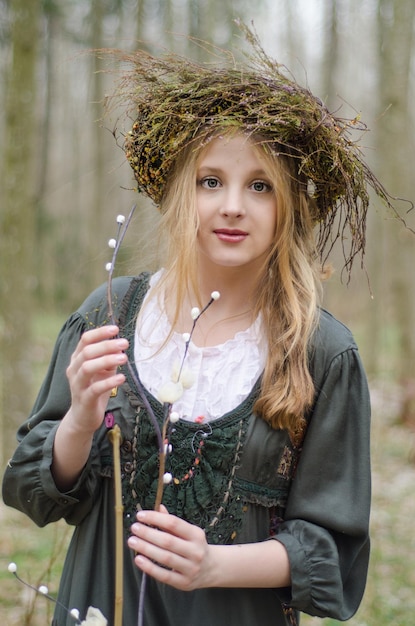 Porträt eines Mädchens in einem volkstümlichen mittelalterlichen Stil mit einem Blumenkranz, der einen Weidenzweig berührt
