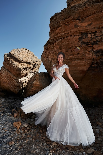 Porträt eines Mädchens in einem wunderschönen Hochzeitskleid, das einen Fotografen am Strand aufwirft.