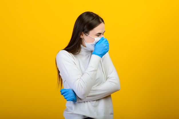 Porträt eines Mädchens in einer medizinischen Maske, die einen Gummihandschuh anzieht. Gelber und grauer Hintergrund. Platz kopieren.