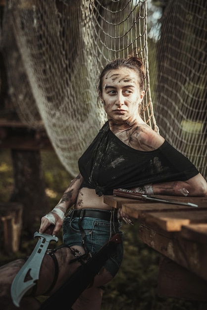 Porträt eines Mädchens in zerrissener Kleidung, das ein Messer hält und im Wald posiert