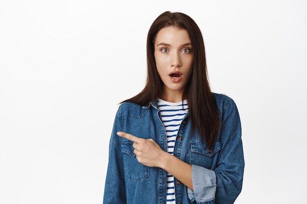 Porträt eines mädchens keucht überrascht, frau sieht mit produkt erstaunt aus, zeigt mit dem finger nach links auf banner, zeigt interessante vorschläge, angebot zum verkauf, weißer hintergrund