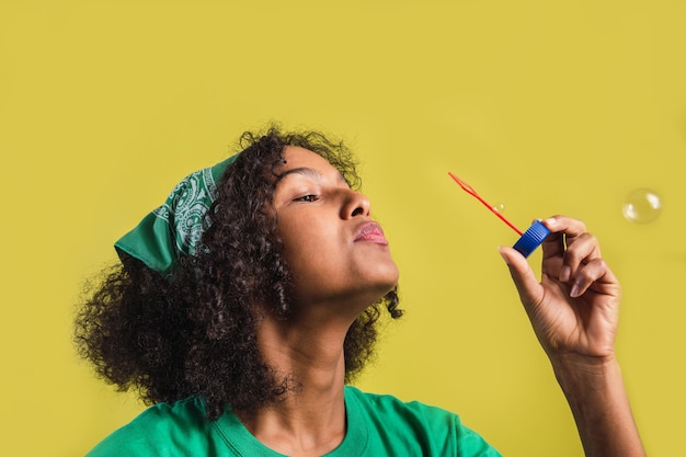 Porträt eines Mädchens mit bläst Luftblasen im Afro-Stil auf gelbem Hintergrund.