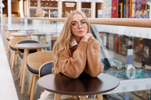 Porträt eines Mädchens mit Brille mit Make-up in einem Einkaufszentrum am Tisch