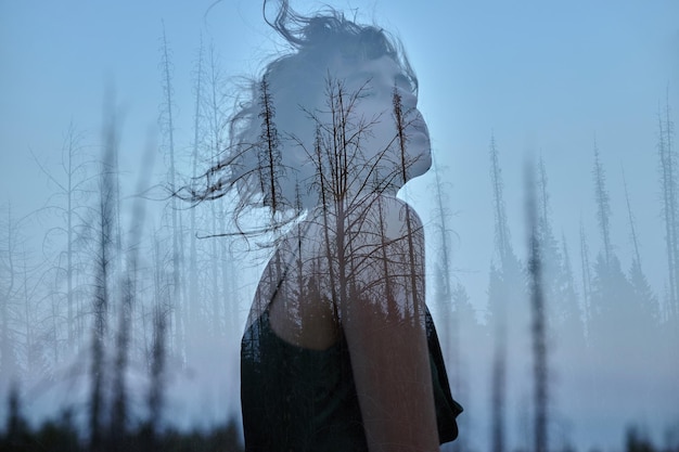 Porträt eines Mädchens mit Doppelbelichtung gegen eine Baumkrone. Zartes mysteriöses Porträt einer Frau mit blauem Himmel in Holz