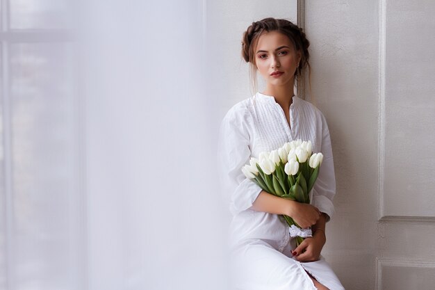 Porträt eines Mädchens mit weißen Tulpen. Schönes Make-up und Frisur. heller Fotoweißhintergrund