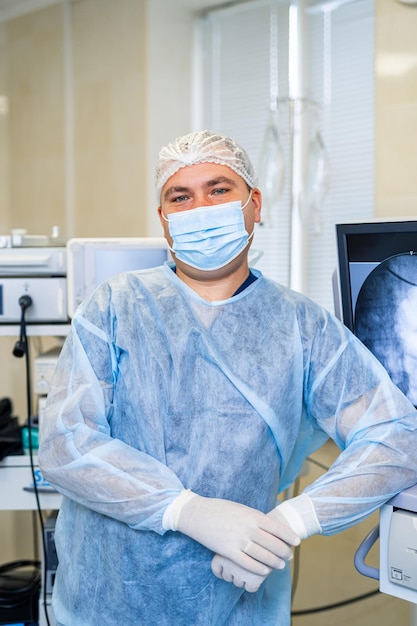 Porträt eines männlichen Chirurgen im Operationssaal, der in die Kamera blickt. Arzt in Peelings und medizinischer Maske im modernen Krankenhaus-Operationssaal
