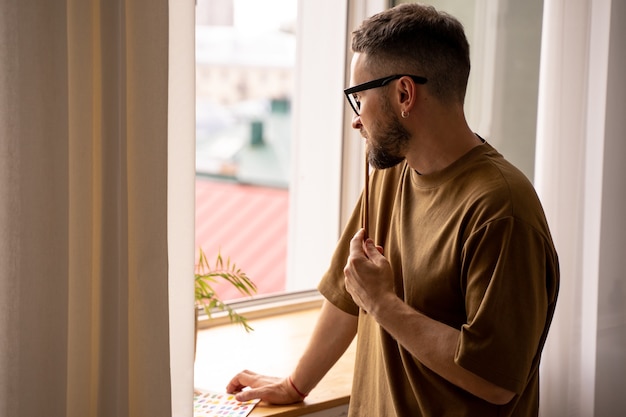 Porträt eines männlichen Künstlers, der aus dem Fenster schaut und nach Inspirationscoaching in Malkursen im Studio sucht, der eine Lektion für Studenten gibt. Pinsel in der Hand. Lebensstil. Echte Emotionen.