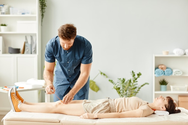 Porträt eines männlichen Physiotherapeuten, der einer jungen Frau Klebeband auf die Knie legt, um Muskel- und Gelenkschmerzen zu lindern