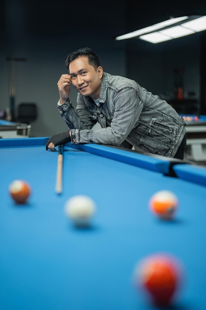 Foto porträt eines männlichen pool-spielers, der seine hand auf den pool lehnt und lächelt