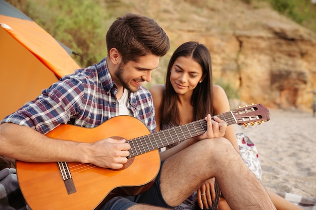 Porträt eines Mannes, der Gitarre für seine Freundin spielt, die im Campingzelt sitzt