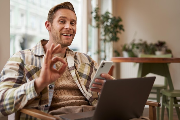 Porträt eines Mannes, der sein positives Feedback gibt, zeigt eine okay-ok-Geste, der mit einem Laptop-Café-Besucher sitzt