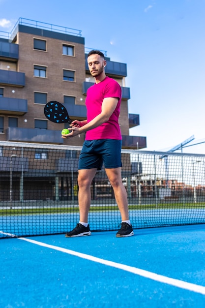 Porträt eines Mannes, der vor der Kamera posiert und bereit ist, auf einem Straßenplatz eine Partie Pickleball zu spielen. Pickleball wird weltweit zu einer sehr beliebten Sportart