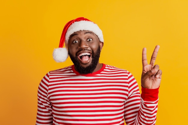 Porträt eines Mannes in Weihnachtsmütze aufgeregtes Gesicht mit offenem Mund zeigen V-Zeichen strahlendes Lächeln auf gelber Wand