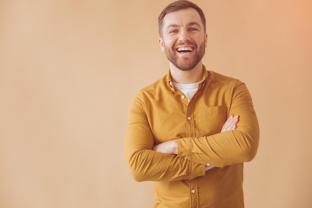 Foto porträt eines modernen millennial bärtigen mannes glücklich und lächelnd in einem gelben hemd auf beige hintergrund