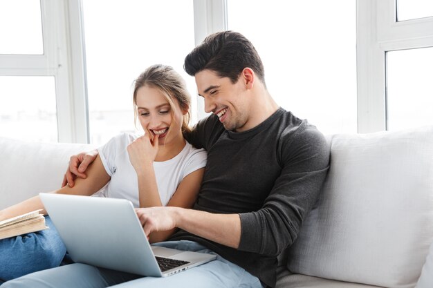 Porträt eines modernen Paares Mann und Frau mit silbernem Laptop beim Sitzen auf der Couch im hellen Raum zu Hause