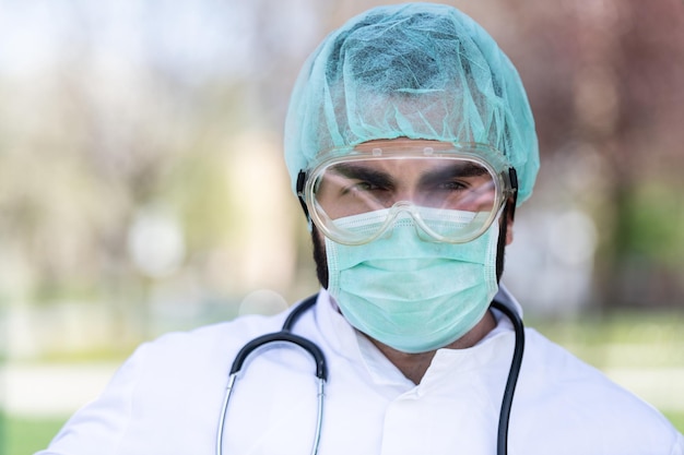 Porträt eines müden, erschöpften männlichen kaukasischen Arztes vor einem Park - Coronavirus Covid-19 Virus Disease - Globaler Pandemieausbruch
