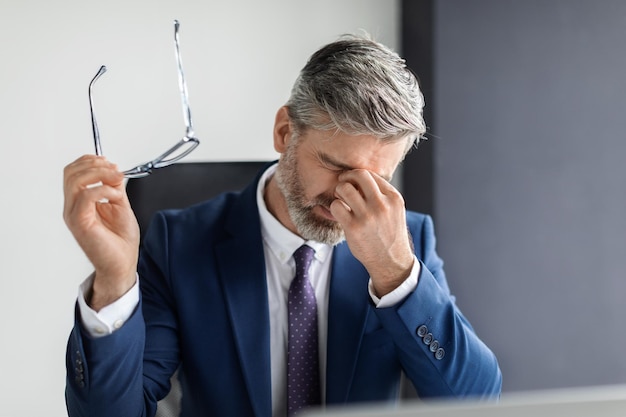 Porträt eines müden Geschäftsmannes mittleren Alters, der am Arbeitsplatz unter Augenbelastung leidet